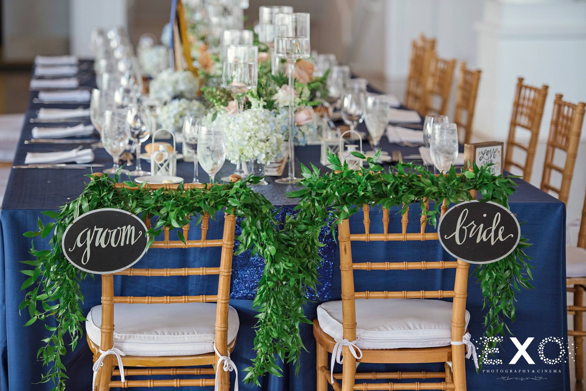 bride and groom chairs at head of table covered in flowers by rori arrangements