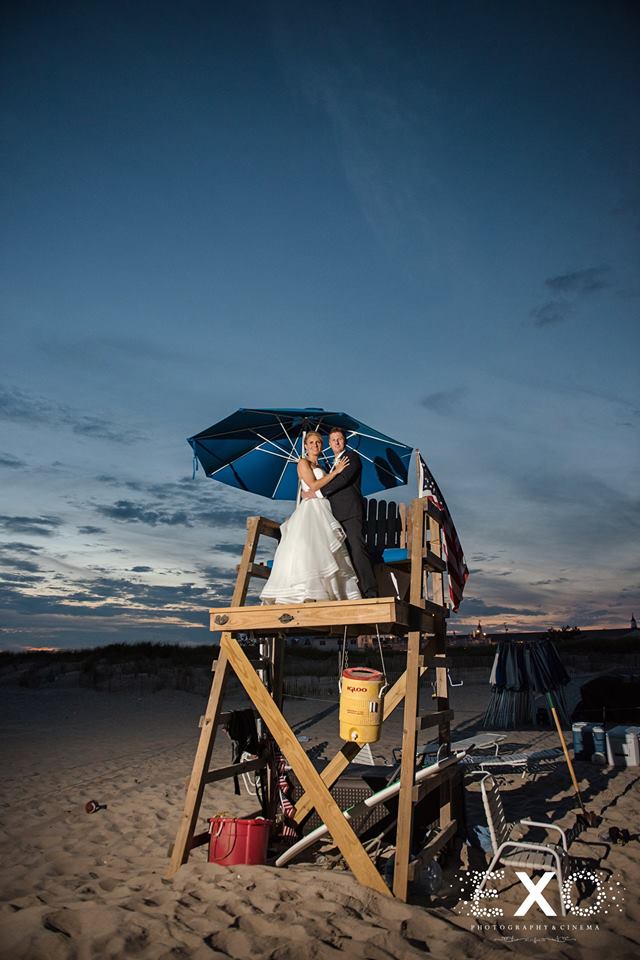 Bride and groom standing on lifeguard stand on beach near Oceanbleu