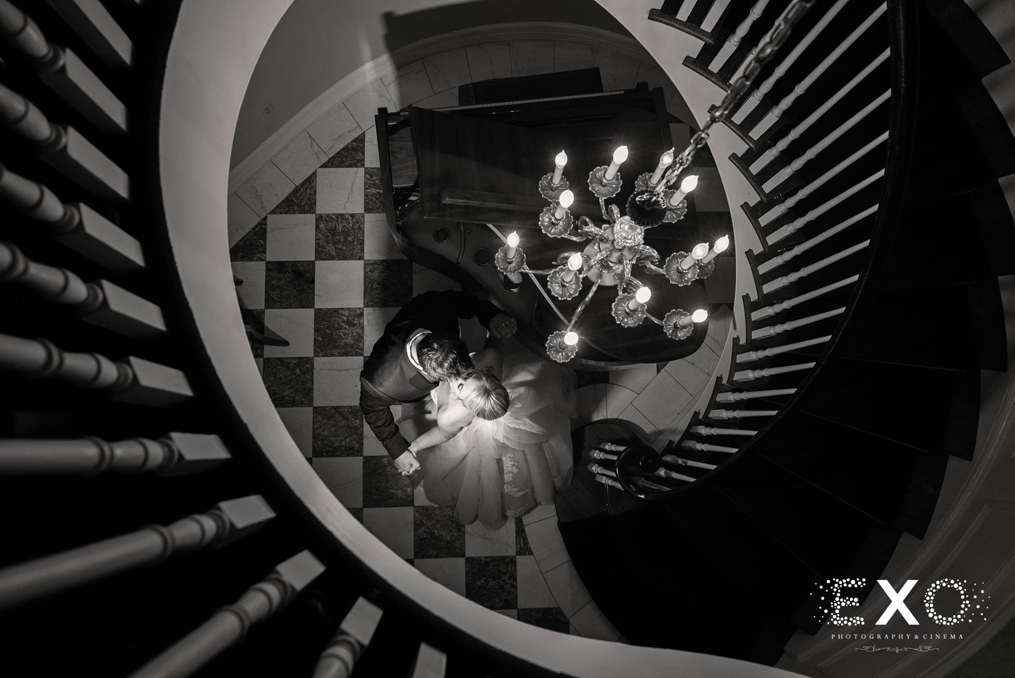 black and white shot from above of bride and groom kissing near staircase at royalton mansion