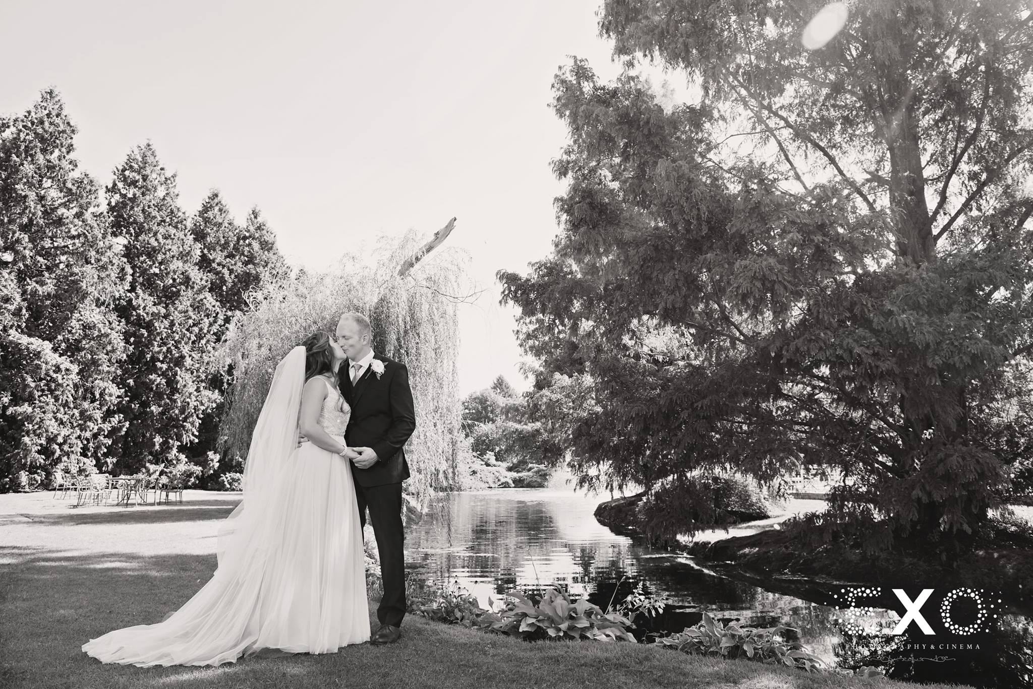 black and white image of bride and groom by water at Flowerfields Celebrations
