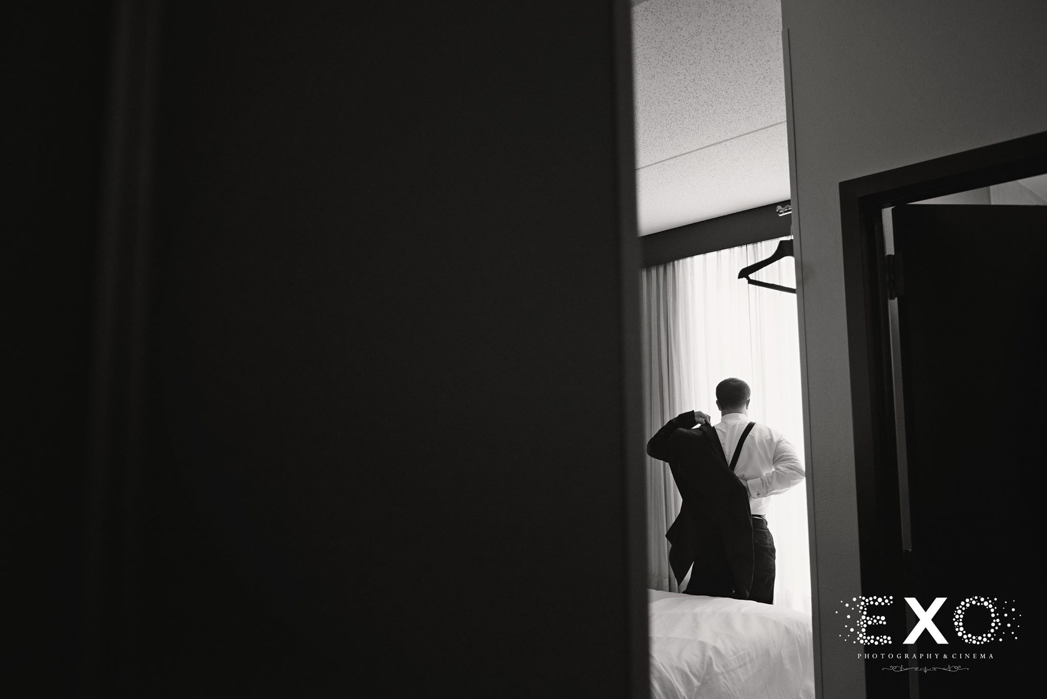 black and white image of groom putting on jacket before ceremony