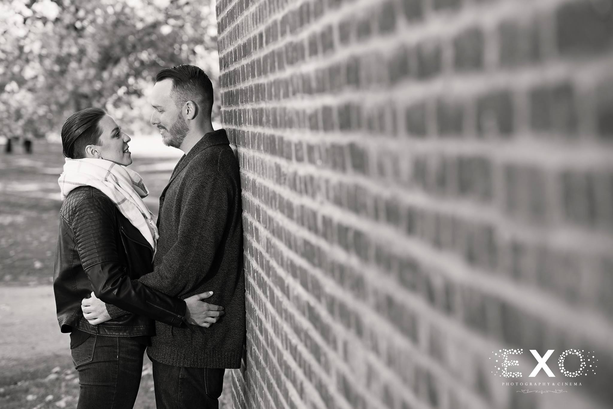 black and white shot of couple by brick wall 