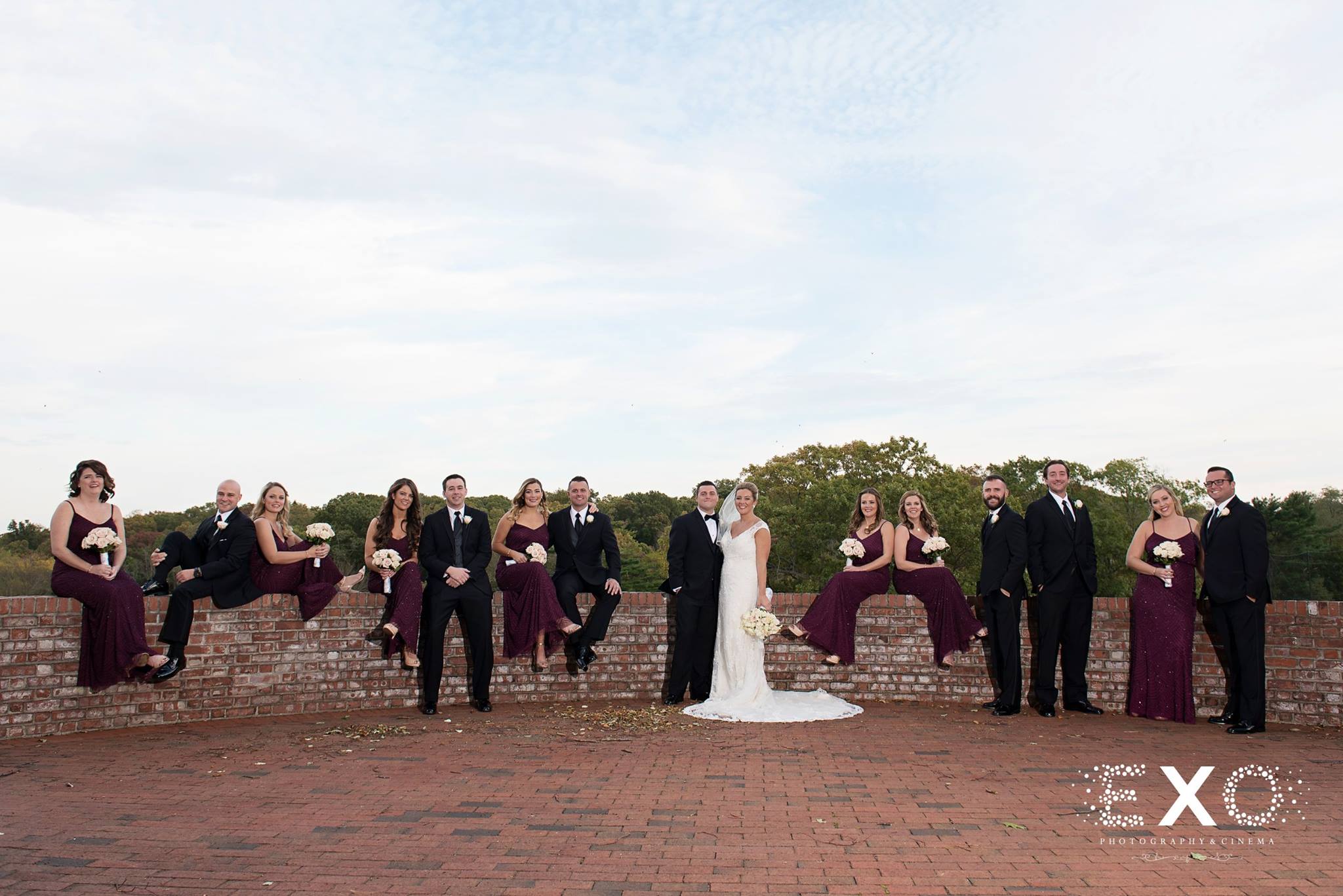 bride, groom, and wedding party sitting on brick wall