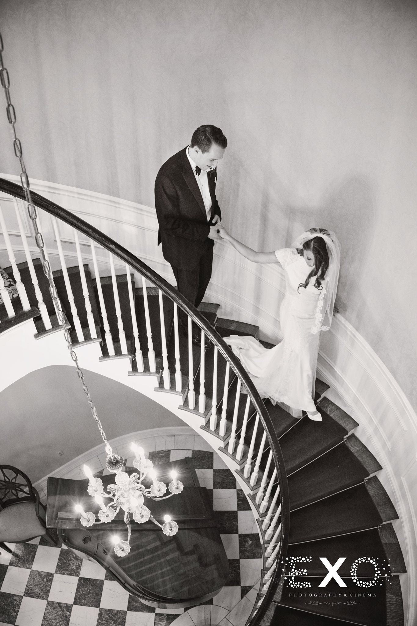 black and white image of bride leading groom down royalton mansion stairs
