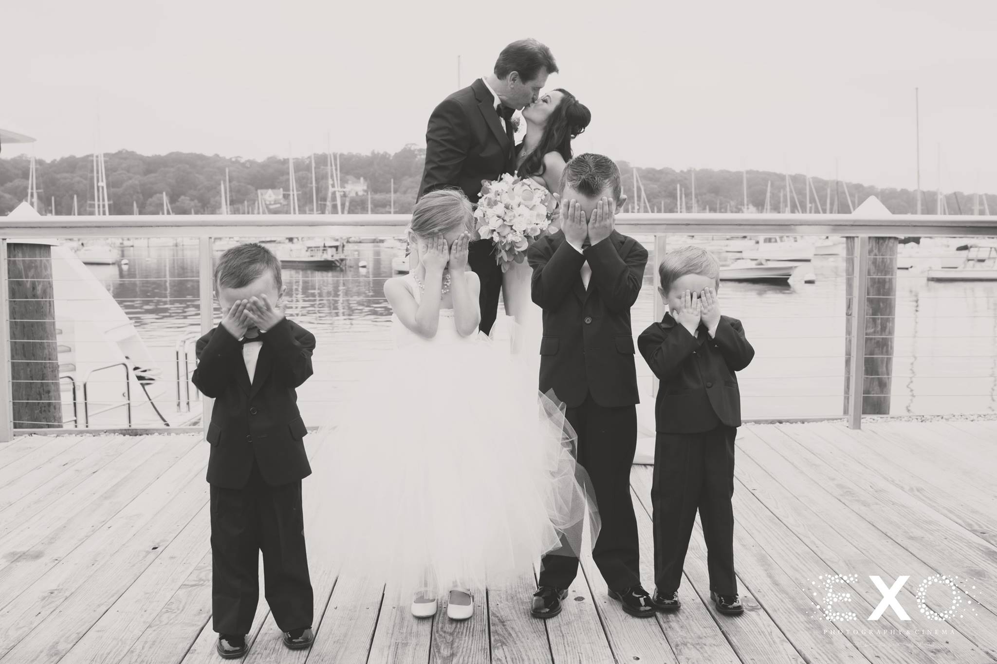 black and white image of bride and groom kissing behind children on dock