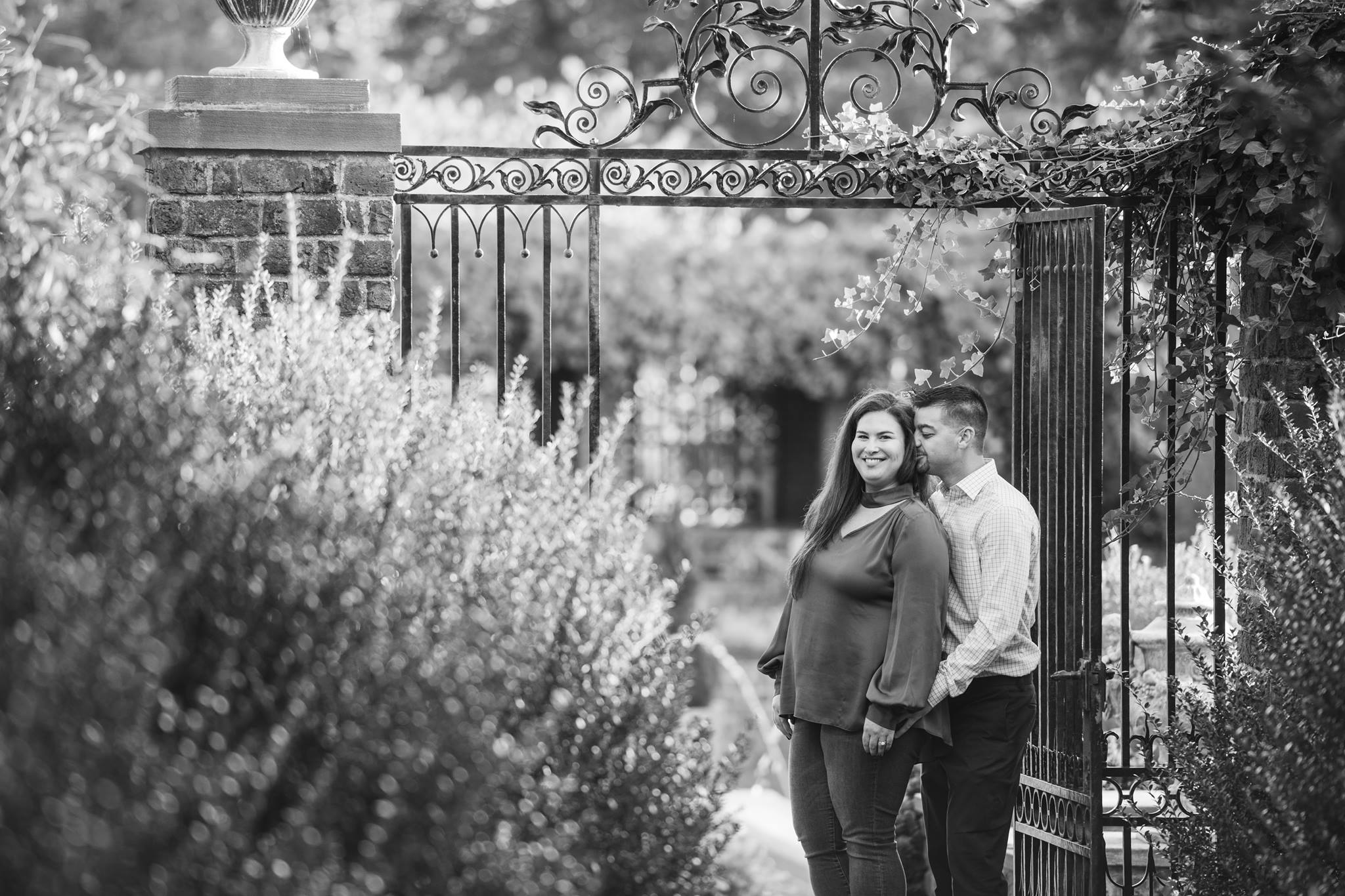 black and white image of couple near tall gate