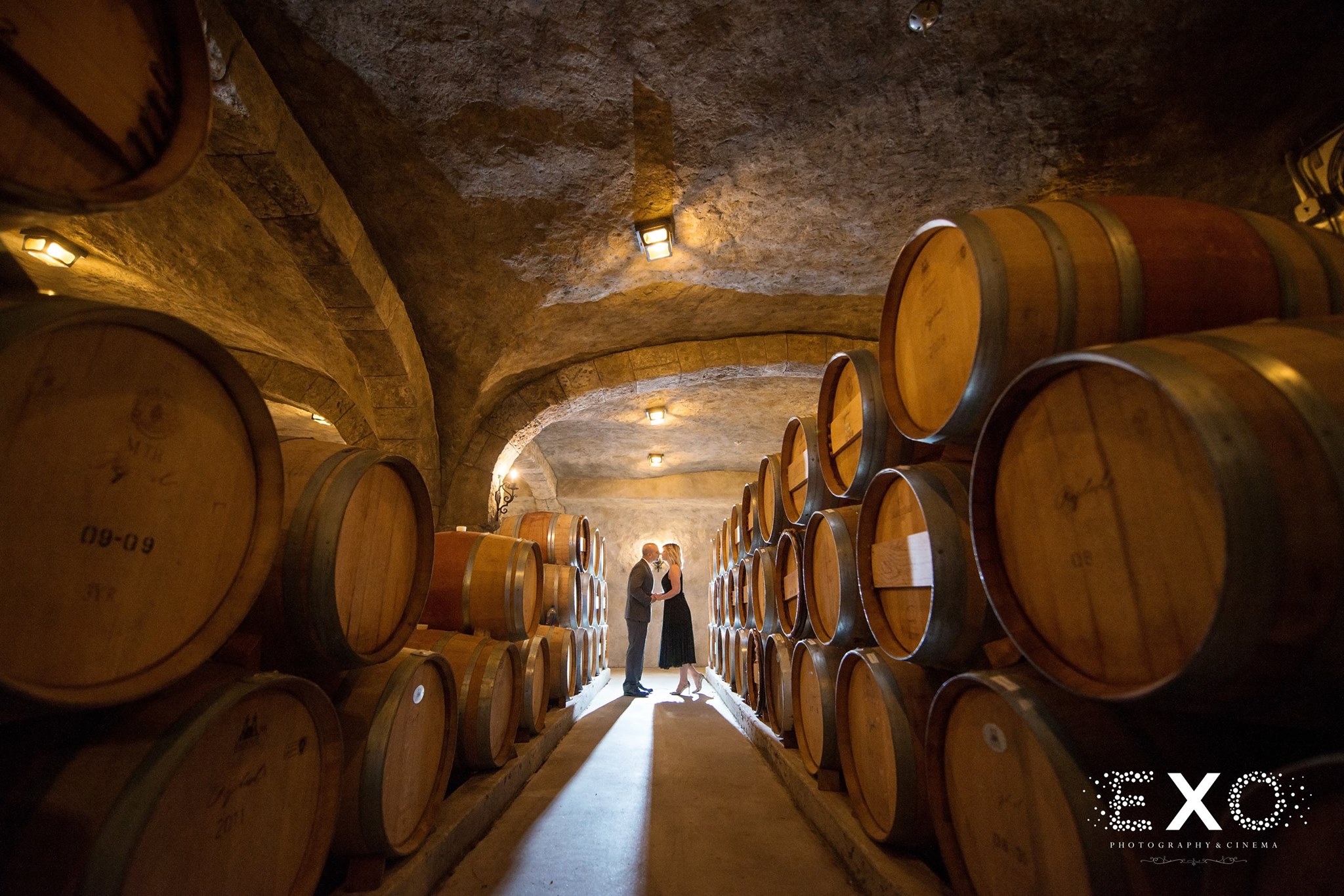 perspective shot of couple kissing down aisle of wine barrels at Raphael Vineyard engagement session