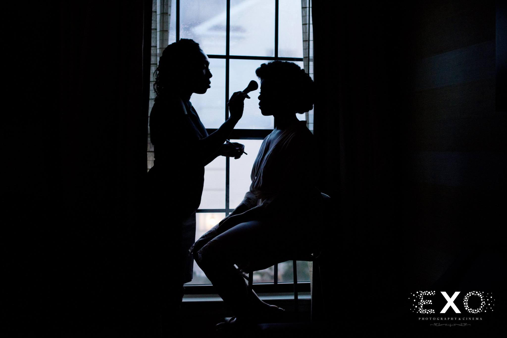 silhouette shot of bride in widow getting makeup done at Fox Hollow