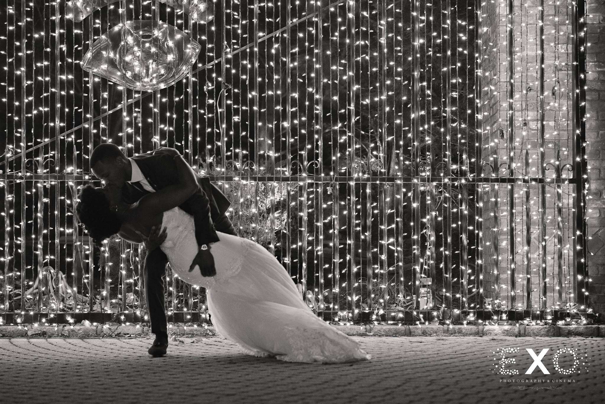 black and white image of bride and groom kissing in a dip near string lights at Long Island wedding