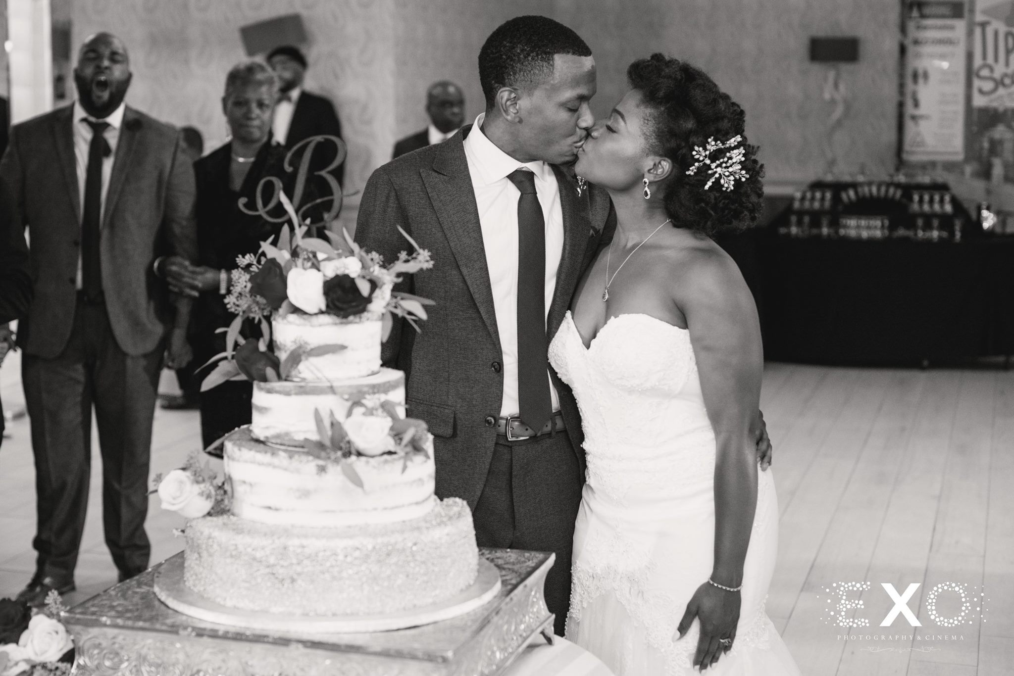 black and white image of bride and groom kissing near wedding cake