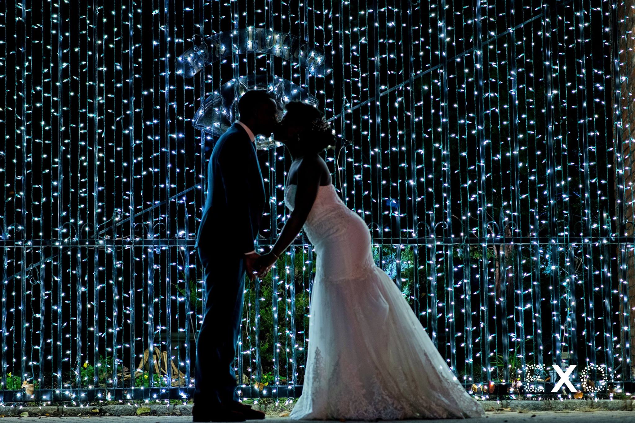 dark image of bride kissing groom near blue string lights at Fox Hollow wedding 