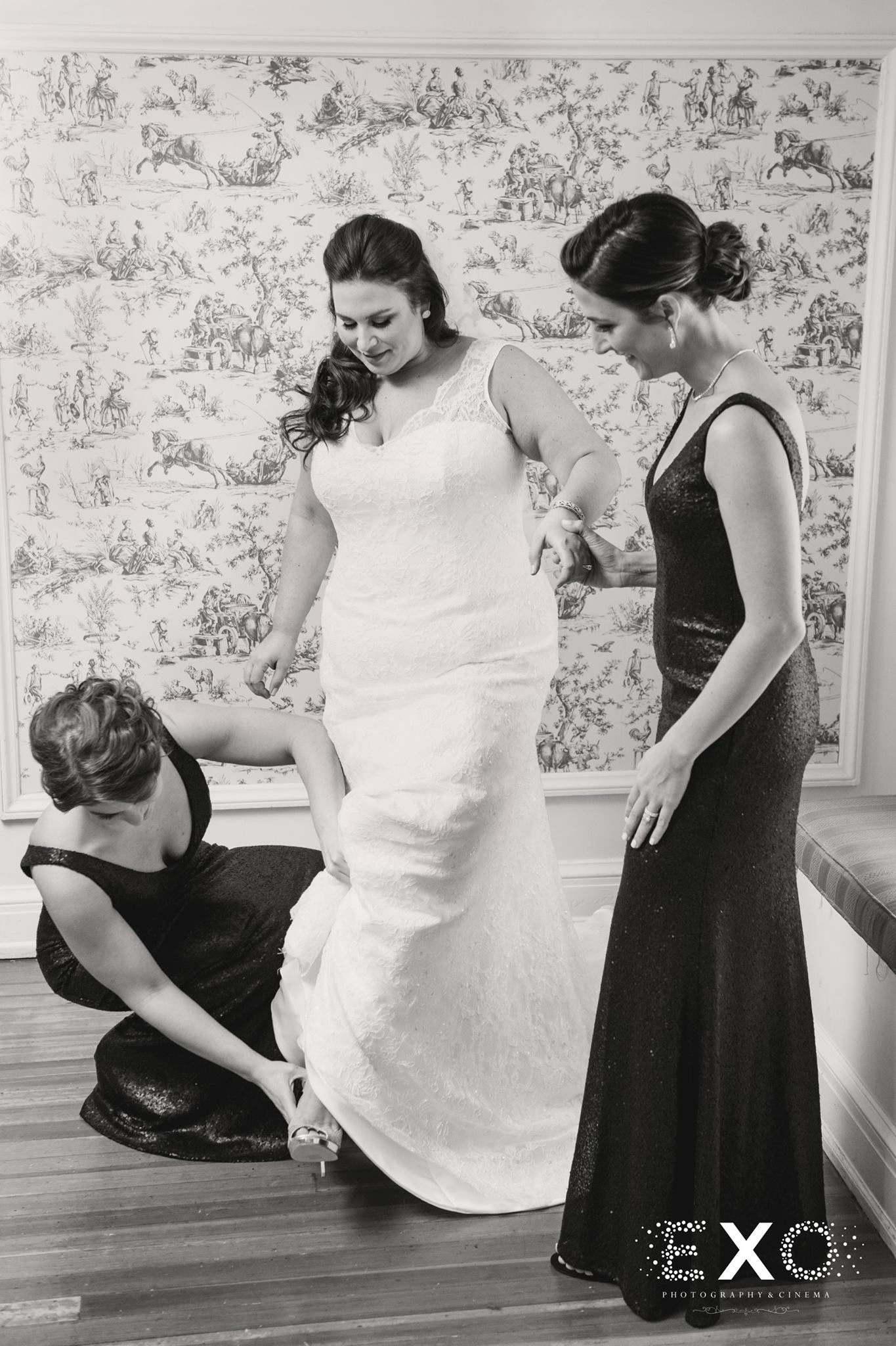 black and white image of bridesmaids helping bride put on jimmychoo bridal shoes
