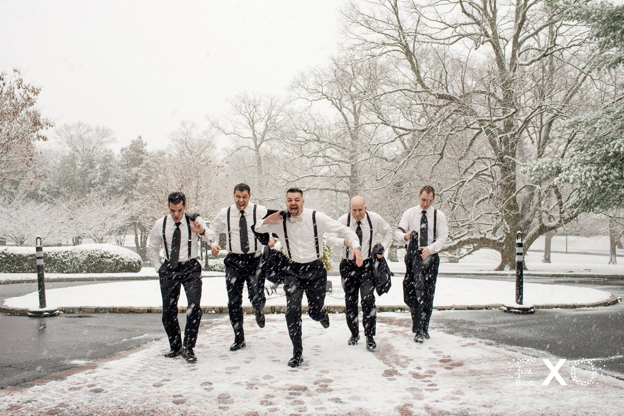 groom and groomsmen running through snow outside Royalton at Roslyn mansion in Foresto Tuxedo rentals