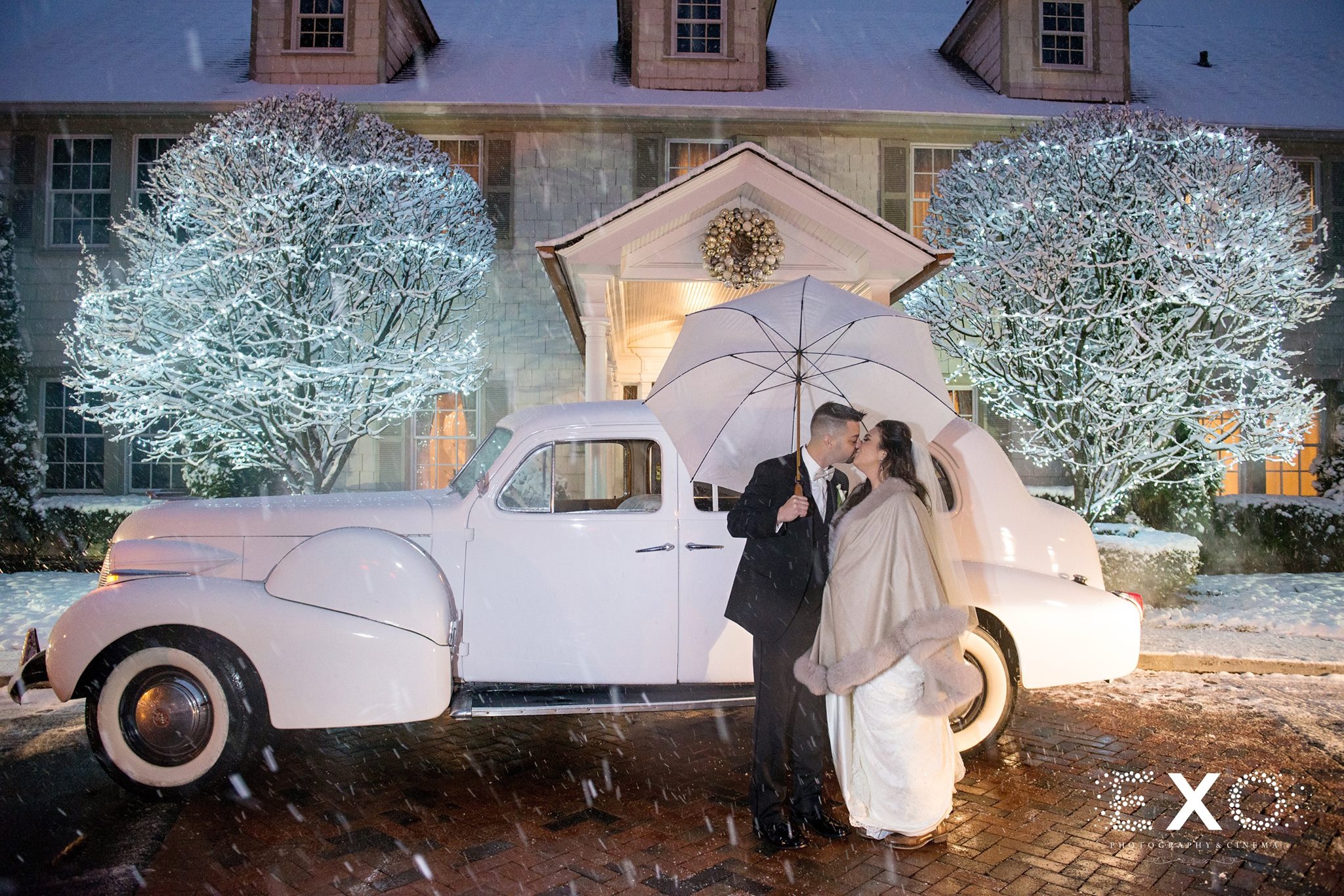 bride and groom standing outside Royalton at Roslyn mansion with car by Camelot Specialty Limo during winter wedding