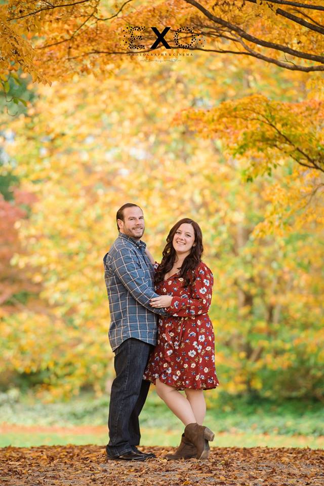 Couple standing between trees with fall leaves at Planting Fields Arboretum