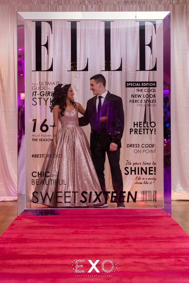 Elle and guest posing in front of magazine backdrop