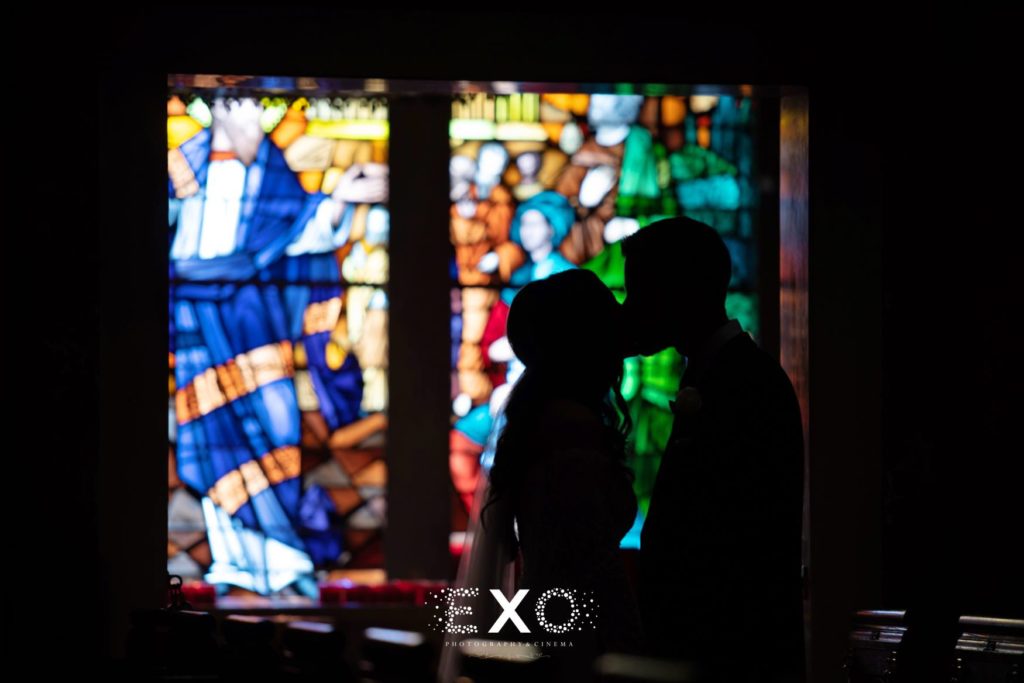 Bride and groom kissing in front of stained glass windows