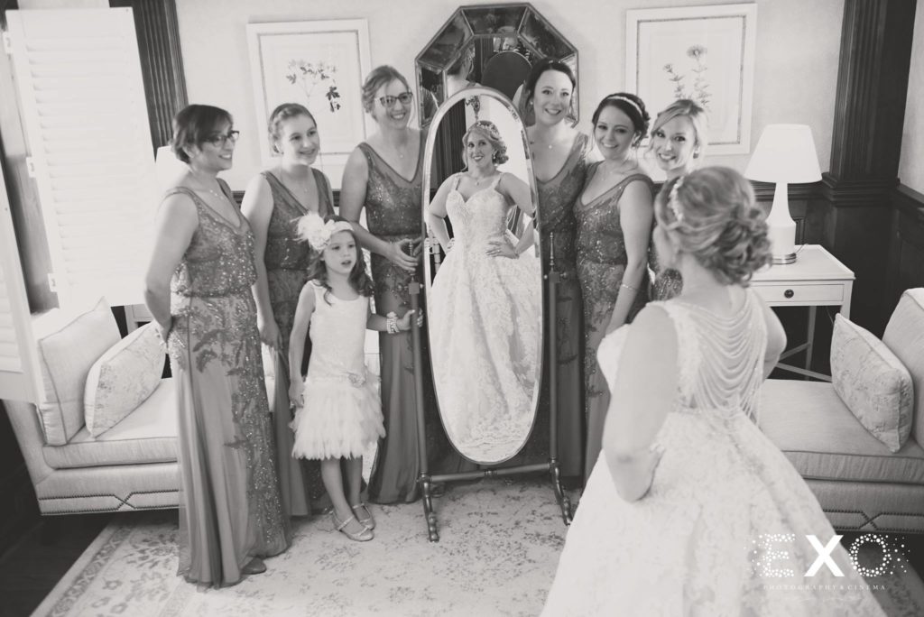 bride looking in mirror with bridesmaids and flower girl onlooking