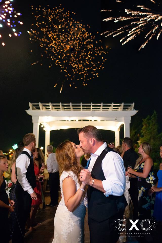 bride and groom kissing with fireworks at Lombardi's on the Bay