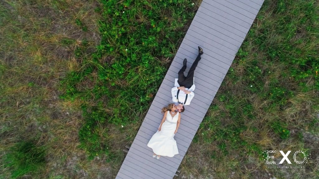 bride and groom laying on boardwalk, drone view