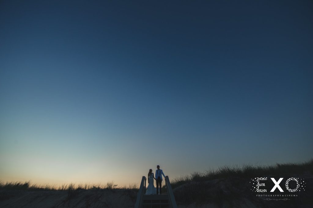 bride and groom holding hands on boardwalk during sunset at Oceanbleu