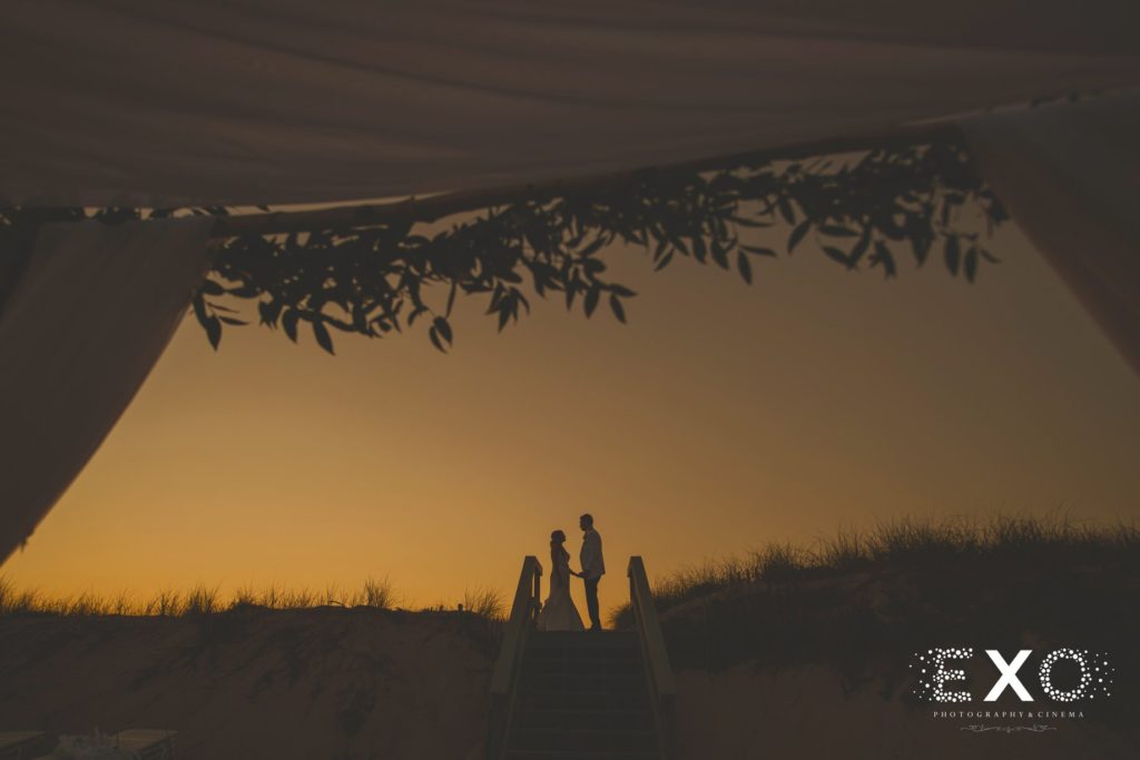 bride and groom standing on the boardwalk during sunset at Oceanbleu