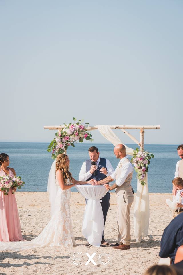bride and groom with flower archway exchanging vows on the beach at Pavilion at Sunken Meadow