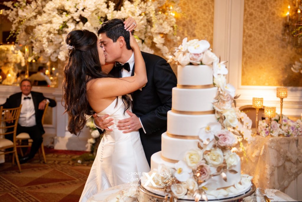 Bride and groom kissing with wedding cake at The Garden City Hotel