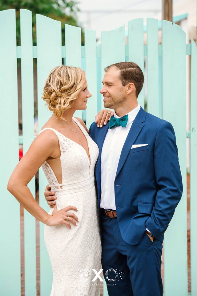 bride and groom posing in front of turquoise fence