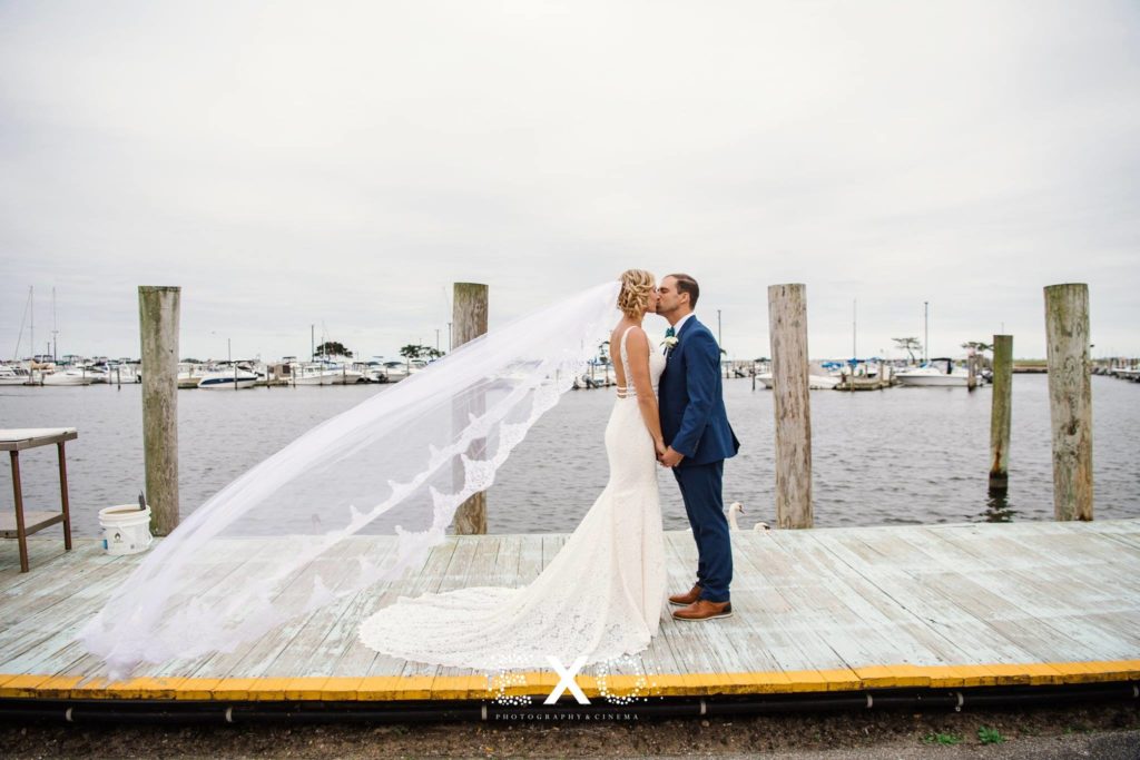 bride and groom kissing on dock with her veil blowing at Captain Bills