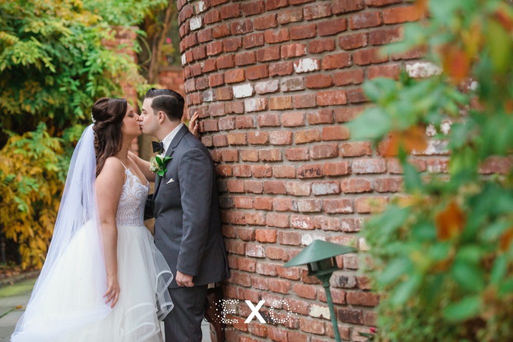 bride and groom kissing against brick wall outside Fox Hollow