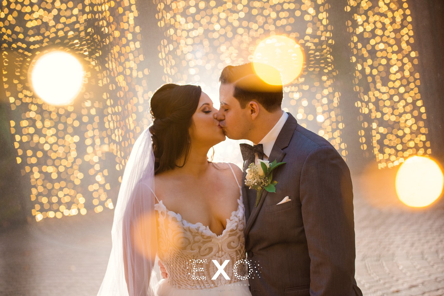 Bride and groom kissing with string light behind them