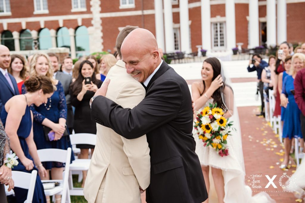 bride's father hugging the groom with bride laughing