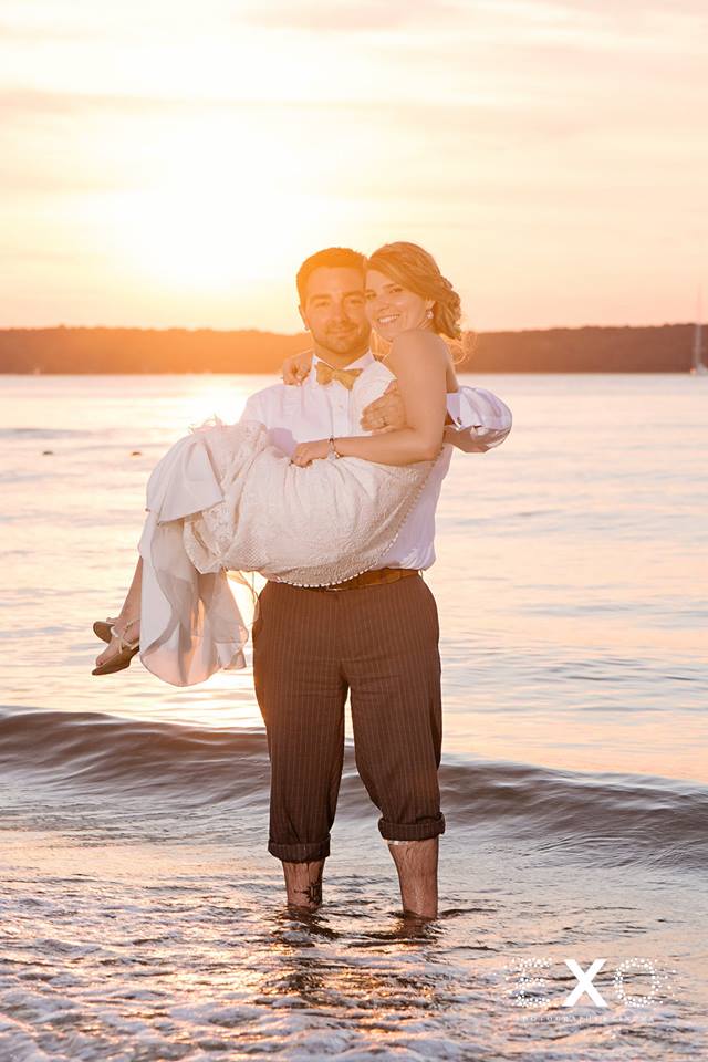 groom holding his bride in the water at sunset at The Head of the Bay Club