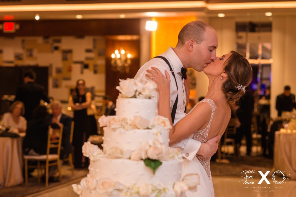 bride and groom kissing by cake at Temple Beth Torah
