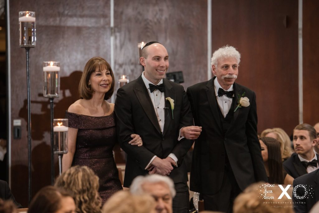 groom and his parents walking down the aisle