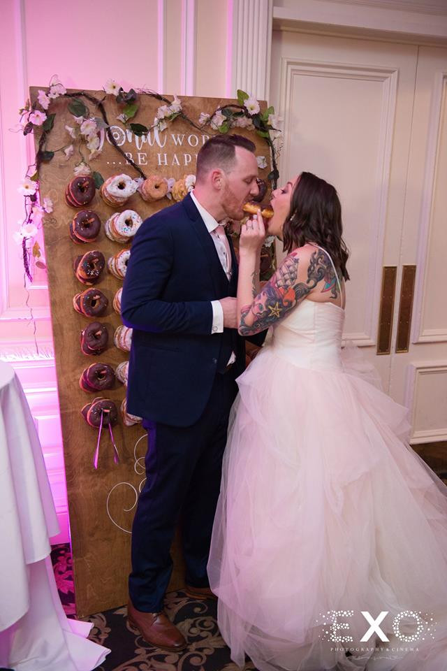 bride and groom sharing a donut from their donut wall