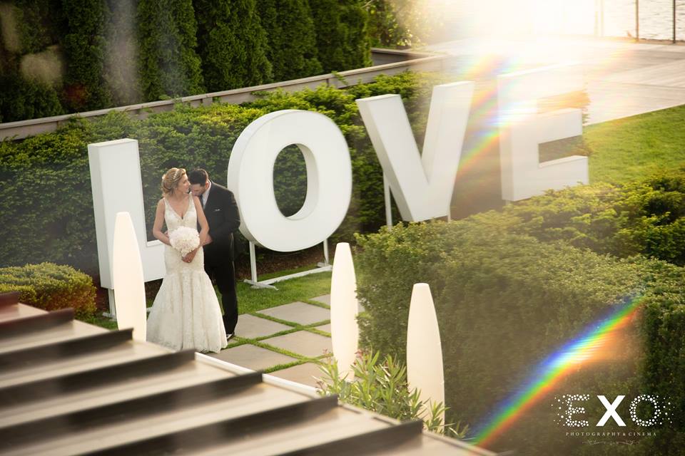 bride and groom by LOVE sign outside Harbor Club at Prime
