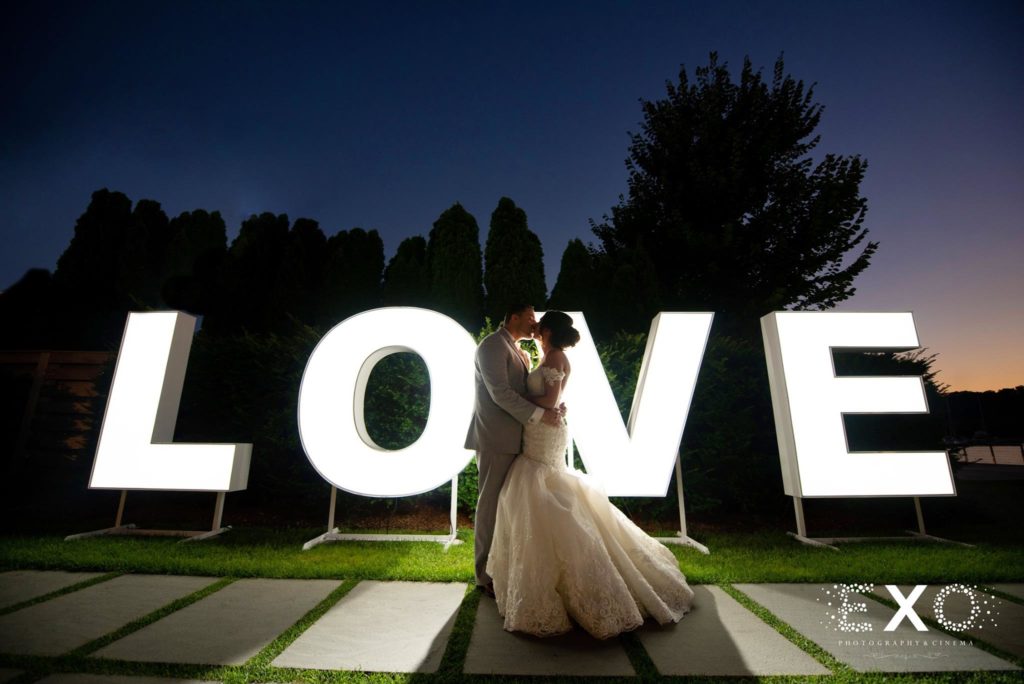 bride and groom kissing by LOVE sign at night at Harbor Club at Prime