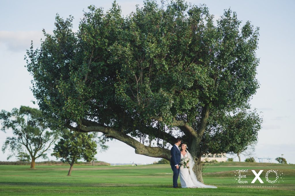 bride and groom posing by the giant tree at Mansion at Timber Point