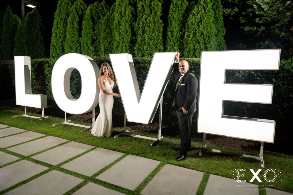bride and groom standing at the LOVE sign outside Harbor Club at Prime