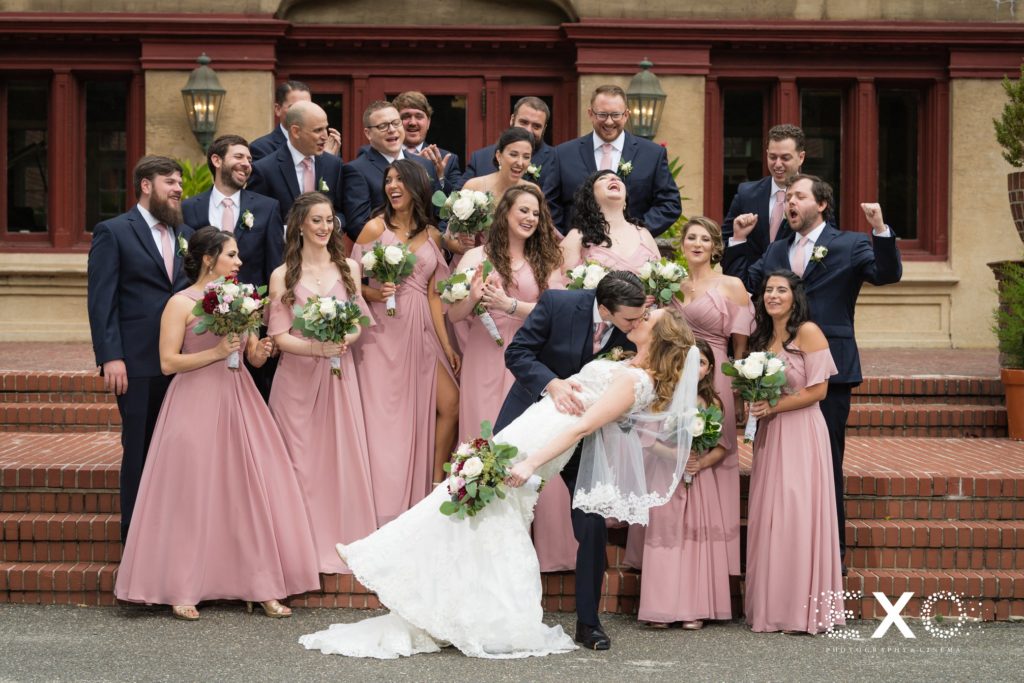 bride and groom kissing in front of their bridal party outside Coindre Hall