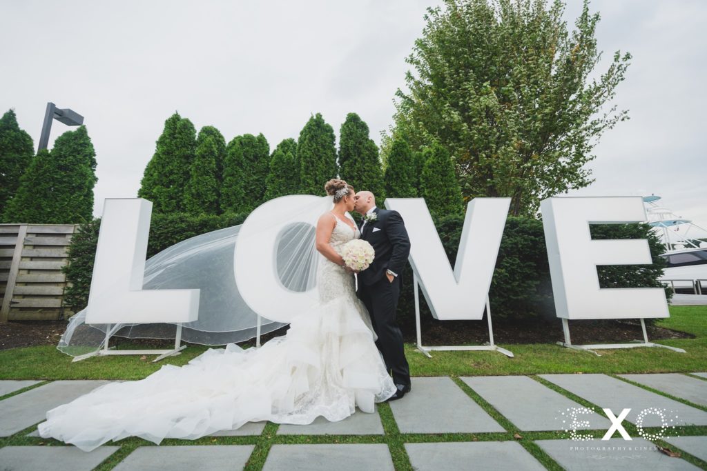 bride and groom kissing in front of the LOVE sign outside Harbor Club at Prime