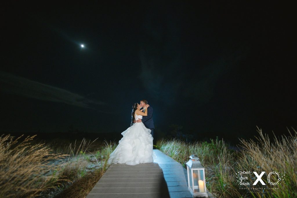 bride and groom kissing on boardwalk at night at Oceanbleu