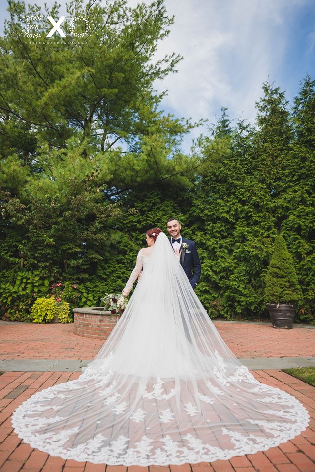 bride's stunning veil spread out while posing with groom outside Crest Hollow Country Club
