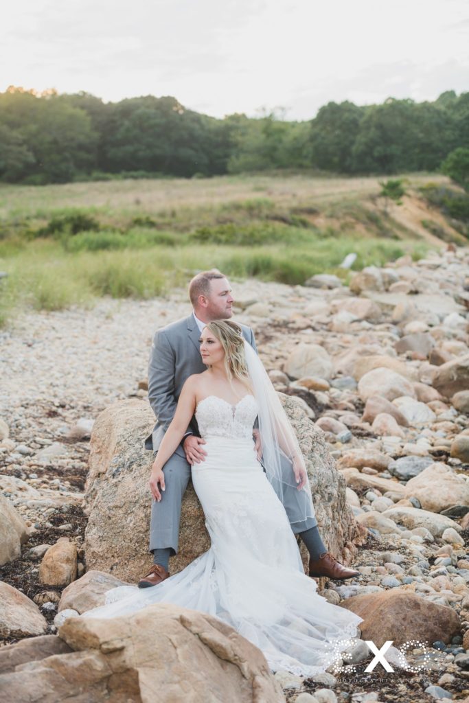 bride and groom sitting on the rocks on the beach at 360 East