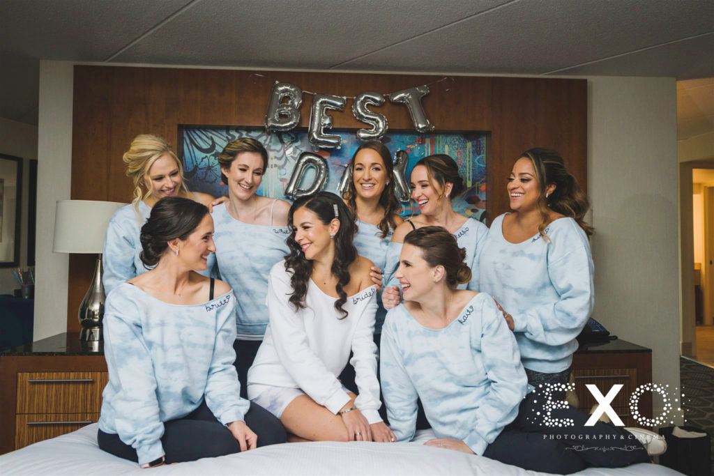 Bridesmaids in sweatshirts on the bed at the hotel