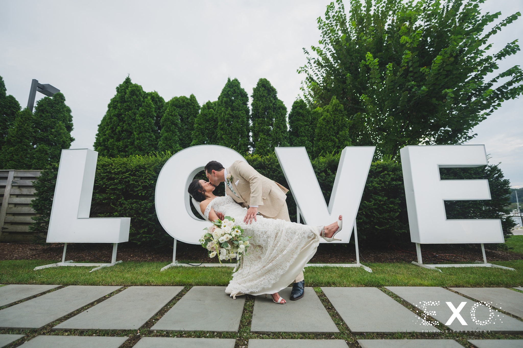 bride and groom kissing in front of love sign