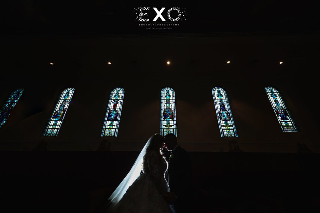 bride in groom in front of church stained glass