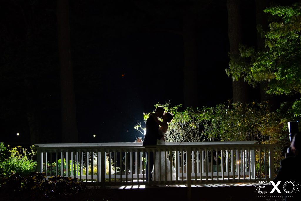 Bride and groom outside at night kissing on bridge. 